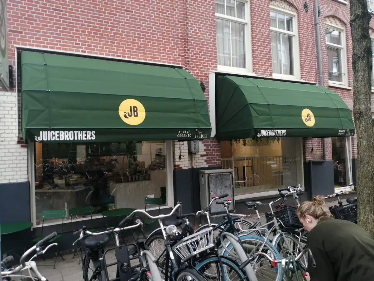 Twee donkergroene markiezen met Juice Brothers-logo boven een juicebar in Amsterdam